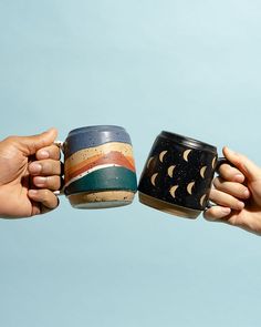 two hands holding cups with different designs on them