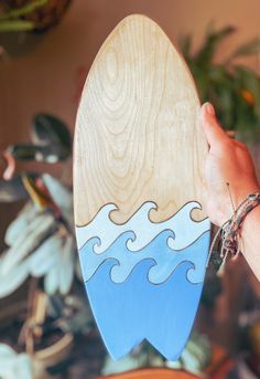 a hand holding a wooden surfboard with blue waves painted on the front and sides