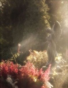 an angel statue standing in the middle of a garden with flowers and trees behind it