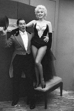 a man standing next to a woman in front of a mirror with her leg on a chair