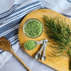 herbs and spoons sit on a cutting board next to a bowl of green powder