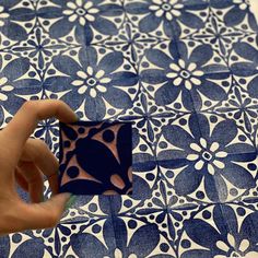 a hand holding a square object in front of a blue and white pattern