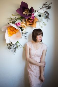 a woman standing in front of a wall with flowers hanging on it's side