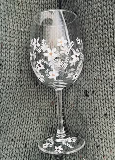 a wine glass sitting on top of a table next to a knitted blanket with flowers painted on it