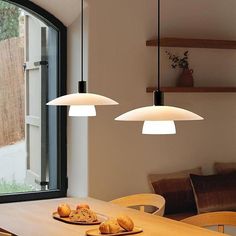 two lights hanging over a wooden table in front of a window with an outside view