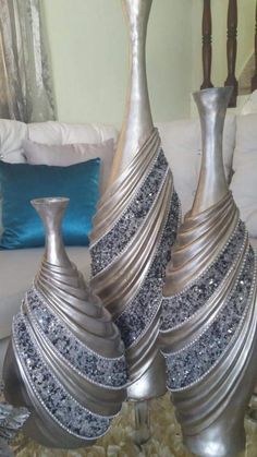 two silver vases sitting on top of a table next to each other in front of a white couch