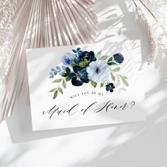 a white card with blue flowers and greenery on it next to some palm leaves