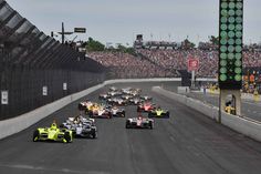 a group of racing cars driving down a race track in front of a large crowd