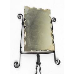 an old fashioned mirror on a stand with wrought iron legs and a metal plate attached to it