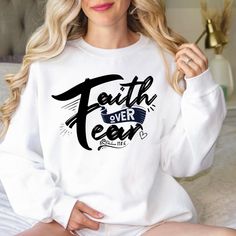 a woman sitting on a bed wearing a white sweatshirt with the words faith over fear printed on it