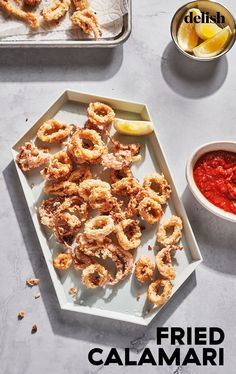 some fried food is on a tray next to a bowl of sauce and lemon wedges