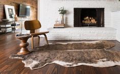 a living room with a white brick fireplace and wood flooring that has a brown rug on it