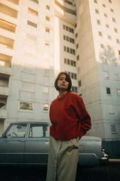 a woman standing in front of a tall building next to a blue car on the street