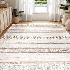 a white and beige area rug in front of a window with potted plants on the side