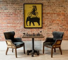 two chairs and a table in front of a brick wall with a poster on it