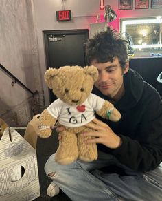 a man is holding a teddy bear in his hands and posing for the camera with it's t - shirt on