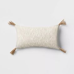 a white and beige pillow with tassels on the front, sitting against a white wall