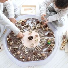 two children are playing with a cake made out of dirt and shells on the table