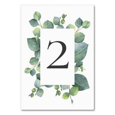 the number two is surrounded by greenery and leaves on a white card with black lettering