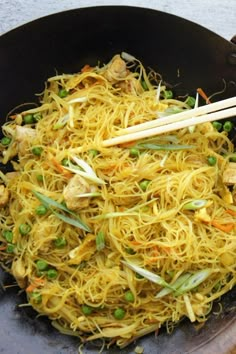 a wok filled with noodles and vegetables next to chopsticks