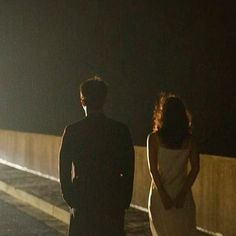 a man and woman standing on the side of a road at night with their back to the camera