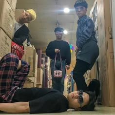 three young men standing and laying on the floor in a room with cardboard boxes all around them