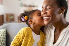 a woman and her daughter are sitting on the couch smiling at each other as they kiss