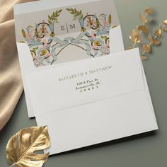 two envelopes with gold foil on them next to a leaf and flower design in the background