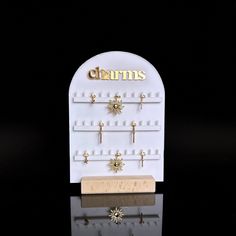 a white display case with earrings on it's sides and the word charms written in gold