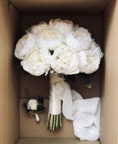 a bouquet of white peonies in a cardboard box with the bride's dress