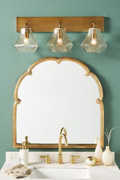 a bathroom vanity with a mirror and three lights on it's side, against a teal green wall