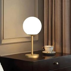 a table lamp sitting on top of a wooden dresser next to a cup and saucer