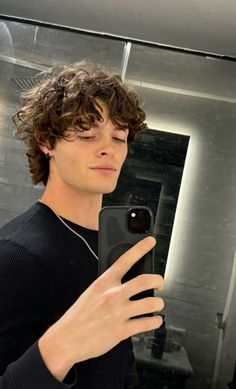 a young man taking a selfie in front of a mirror with his cell phone