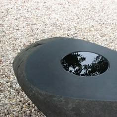 a black object with trees reflected in it on the ground next to gravel and rocks