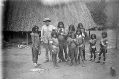 an old black and white photo of people standing in front of a thatched hut