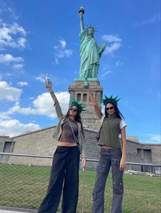 two women standing next to each other in front of the statue of liberty holding up their hands