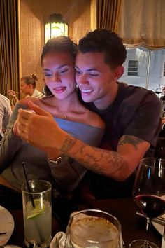 a man and woman sitting at a table looking at a cell phone with their arms around each other