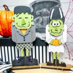 two paper cutouts of people dressed as zombies on a table with pumpkins in the background