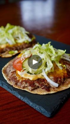 two hamburgers with lettuce and tomato on them sitting on a slate board