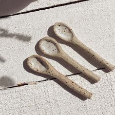 three wooden spoons sitting next to each other on a white surface with shadows from the sun