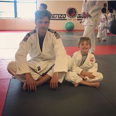 a man sitting on the ground with a child in front of him wearing karate gear