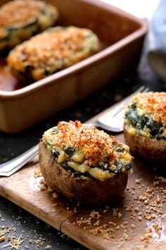 two stuffed mushrooms on a cutting board with a fork next to it and another dish in the background