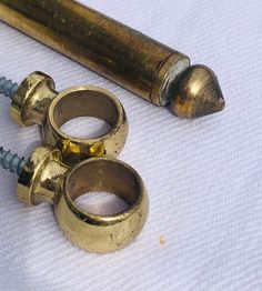 two brass screws sitting next to each other on a white tablecloth with a gold colored object in the background