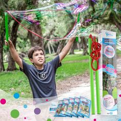 a young boy holding up a kite in the air with other items around him and trees behind him