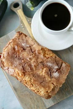 a piece of bread sitting on top of a cutting board next to a cup of coffee