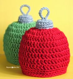 two crocheted red and green hats sitting on top of a yellow table next to each other