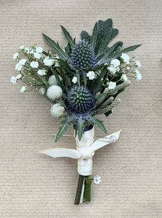 a bouquet of flowers sitting on top of a floor next to a white vase with green leaves