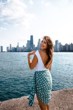 a woman standing on the edge of a body of water with a city in the background