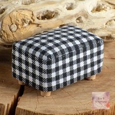 a black and white checkered ottoman sitting on top of a piece of wood next to a log