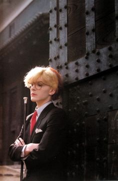 a woman with blonde hair and glasses is holding an umbrella while standing in front of a wall